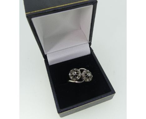 A diamond set crossover Ring, formed of two flowerheads, each with nine small diamonds, mounted on the cross in silver on a p