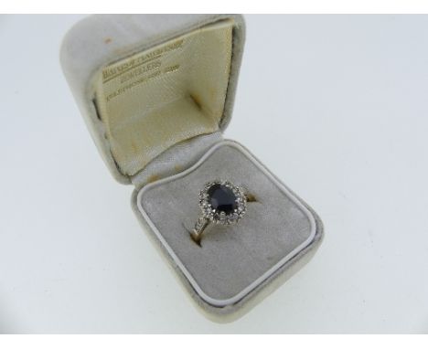 A sapphire and diamond cluster Ring, the oval facetted sapphire surrounded by twelve small diamonds and with two small diamon