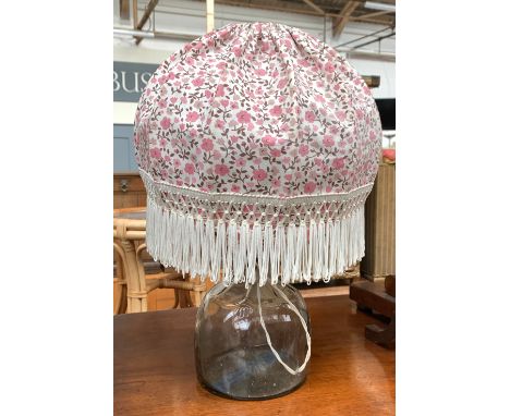 A vintage glass bottle, converted as a table lamp with tasseled shade 