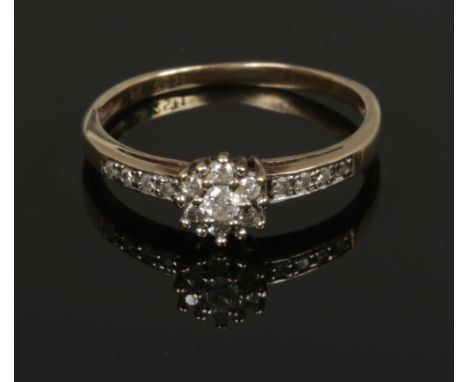 A 9ct gold dress ring with diamond daisy cluster and diamond set shoulders, 0.25ct. Size R.