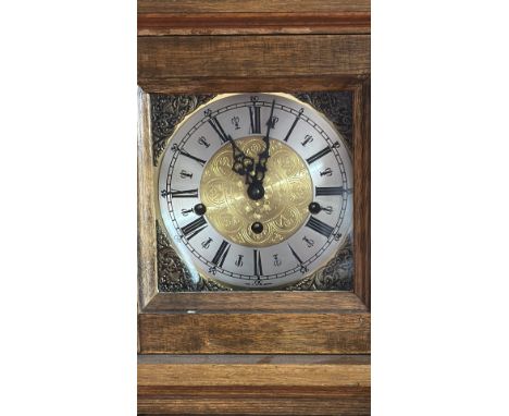 Oak and brass longcase clock features a traditional design with Roman numerals and a glass door that reveals the pendulum and
