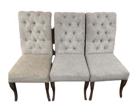 A set of three contemporary high backed dining chairs in grey buttoned fabric with metal ring-handles