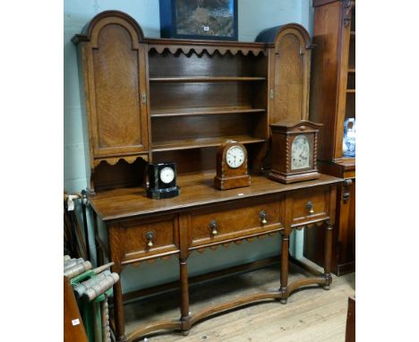 5' 6" Edwardian oak Arts & Crafts dresser with arched cabinet and shelf back standing on a 3 drawer base with cross stretcher