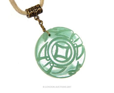 A Chinese, green, circular, carved jade pendant on cream leather thonging, Length: 26 cm.