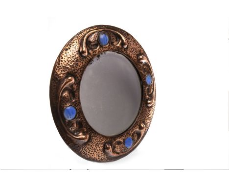 CIRCULAR BEVELLED WALL MIRROR OF LIBERTY DESIGN, contained in a hammered and scroll embossed copper frame inset four ceramic 