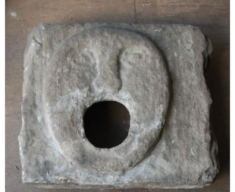 A 16th/17th century STONE CARVED FOUNTAIN HEADthe square panel carved with an oval flattened face with wide mouth, 47 x 48cmT