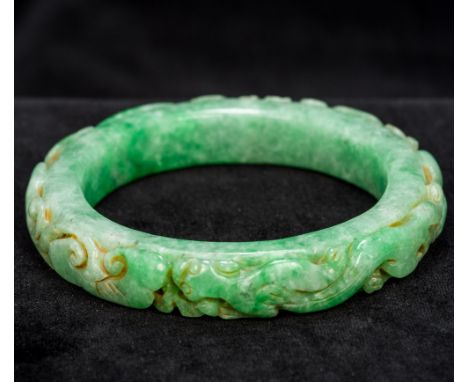 A Chinese carved apple green jade bangleCarved in the round with dragons.  8 cm diameter.  CONDITION REPORTS: Generally in go
