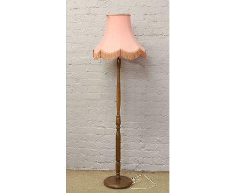 A carved oak standard lamp with pink shade and circular base.