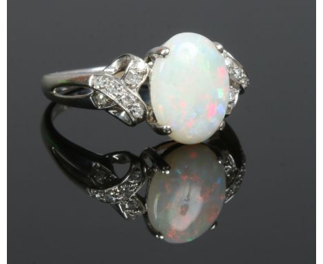 A 9ct white gold opal ring with diamond set open bow form shoulders, size Q.