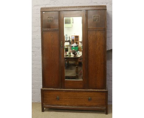 An Edwardian oak mirror front wardrobe with metal mounts raised on a drawer base.