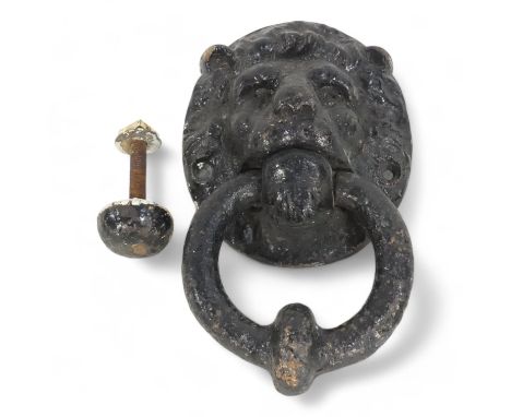 A 19th century cast iron door knocker - modelled as a lion mask holding a ring, together with a button, 19cm high.