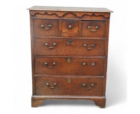 A George III oak chest of drawers - the rectangular top with cusped corners above an arrangement of three short and three lon
