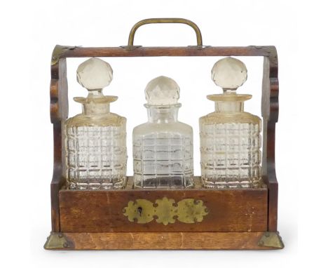 An early 20th century oak tantalus - with brass mounts and three cut glass bottles, 35cm wide.