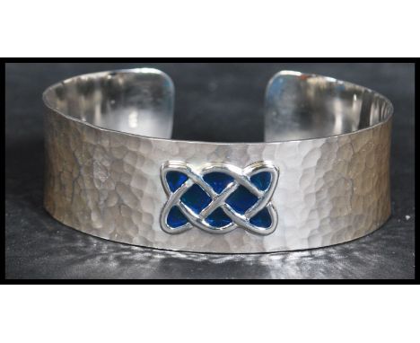 A sterling silver arts and crafts style bangle bracelet having a hammered design with an enamel Celtic knot motif. Weighs 28.