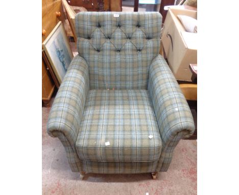 A vintage box framed armchair with green tartan button back upholstery, set on turned front legs with brass caps and casters