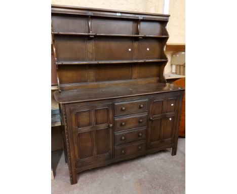 A 1.45m vintage Ercol dark elm two part dresser with two shelf open plate rack over a base with four central drawers and flan