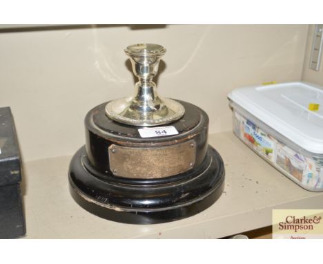 An ebonised trophy plinth with silver plaque and a plated candlestick 