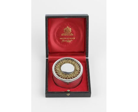 A SILVER AND SILVER GILT CIRCULAR BOX AND COVER, by Stuart Devlin, London 1984, the top with flowerhead design over red ename
