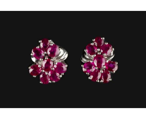 A PAIR OF RUBY CLUSTER EAR STUDS, each designed as a ribbon-shaped cluster of oval mixed-cut rubies in claw settings, on post