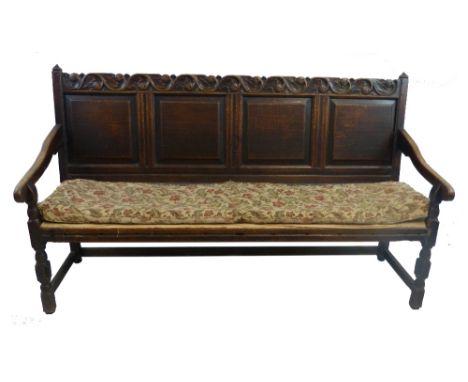 An 18th century oak settle or bench seat, with carved top rail, over four fielded panels and downward sweeping arms, turned s