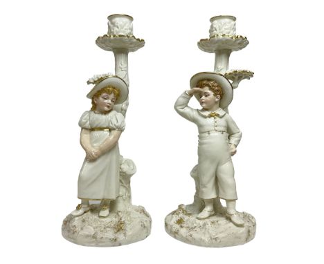 Pair of Royal Worcester figural candlesticks designed by James Hadley in the style of Kate Greenaway, modelled with a young b