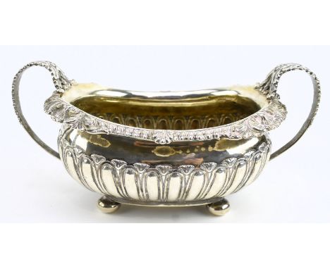 A George III hallmarked silver sugar bowl on four ball feet. The bowl has converging flute decoration on the body, foliate ri
