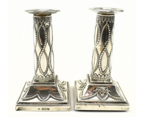 A pair of Edward VII hallmarked silver candlesticks, filled. Each candlestick being decorated with embossed laurel swags, bea
