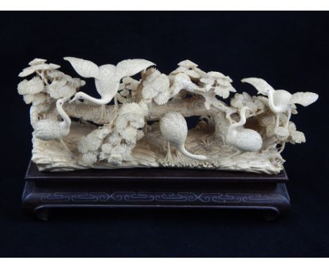 A Japanese ivory carving, 19th century, depicting five cranes before and upon a flowering low branch and naturalistic rocky b