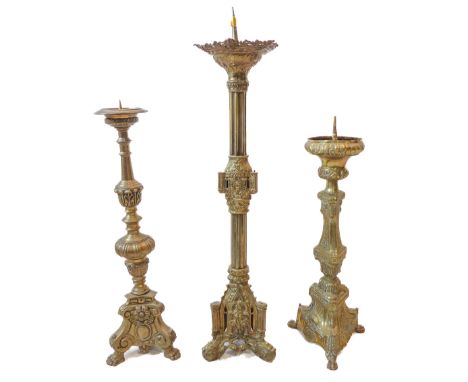 Three continental brass pricket candlesticks: one of Gothic triform with architectural elements; and two decorated with swags