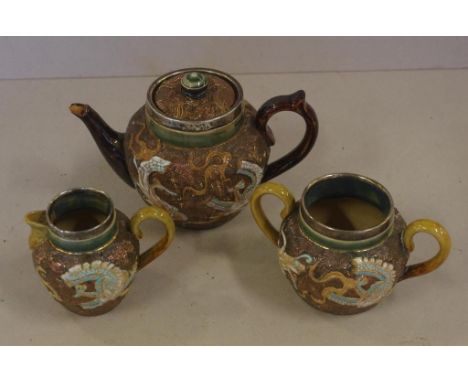 Three piece Doulton Lambeth stoneware teaset with hallmarked silver collar, decorated with dragons in relief, to include teap