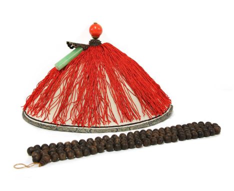 A Chinese official's hat, with a coral ball finial and a hardstone tube ornament, above red tassels covering the circular dom