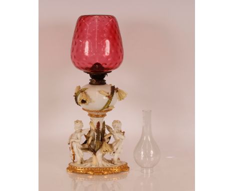 A Moore porcelain table oil lamp, profusely decorated with cherubs playing musical instruments and floral encrusted trailing 