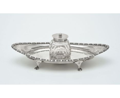 A silver oval inkstand by James Deakin &amp; Sons, Sheffield 1910, with a bead and reel border, on four paw feet, with a cut 