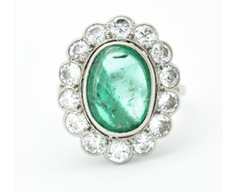 A platinum, emerald and diamond cluster ring. The ring set with an emerald oval cabochon within a halo of round brilliant cut