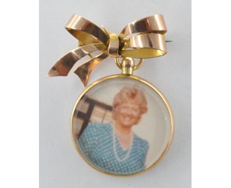 A vintage stamped 9ct gold photo brooch having a gold bow to the top with round photo suspended below. Bow marked 9ct. Bow me