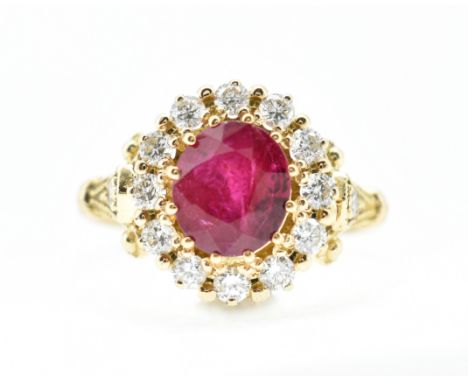 An 18ct gold Burma ruby and diamond cluster ring. The ring set with a central oval cut Burmese ruby surrounded by a halo of r