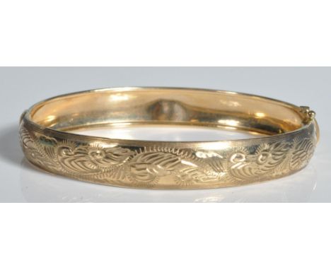 A stamped 375 9ct gold bangle having incised foliate decoration to the exterior with a tongue in groove clasp. Safety chain m