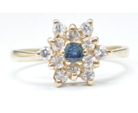 A hallmarked 9ct gold flower head ring set with a central blue stone surrounded by round cut white stones. Hallmarked London 