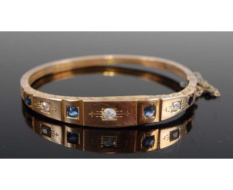 A late Victorian yellow metal, sapphire and diamond set hinge bangle, set with three round cut diamonds each dispersed with a