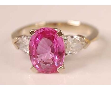 A white metal, pink sapphire and diamond three stone ring, featuring a centre oval faceted pink sapphire with a pear cut diam