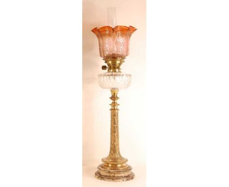 A late Victorian pedestal oil lamp, having a sepia tinted acid etched shade over a cut clear glass font, to a leaf cast brass