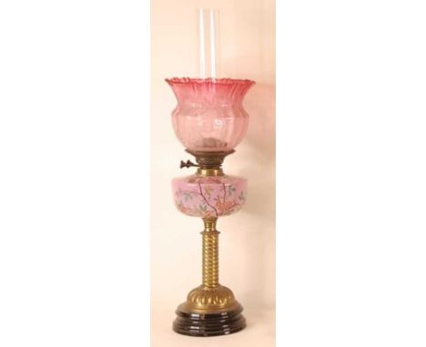 A Victorian pedestal oil lamp, having a cranberry tinted acid etched shade, over a polychrome decorated pink glass font, to a