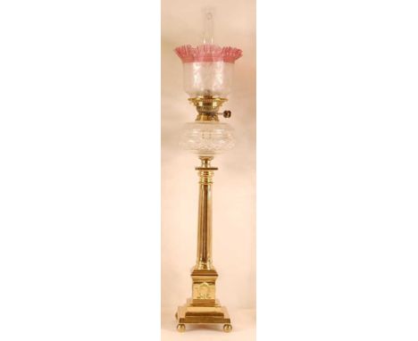 A lacquered brass pedestal oil lamp, having a crinoline cranberry glass and repousee decorated shade, over a cut clear glass 