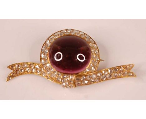 An early 20th century yellow metal bar brooch in the form of a be-ribboned hat, featuring a centre oval cabochon cut garnet w