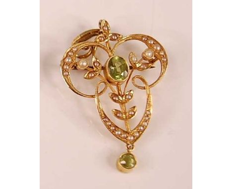 A yellow metal Edwardian peridot and seed pearl openwork pendant featuring a centre oval faceted peridot within a scrollwork 
