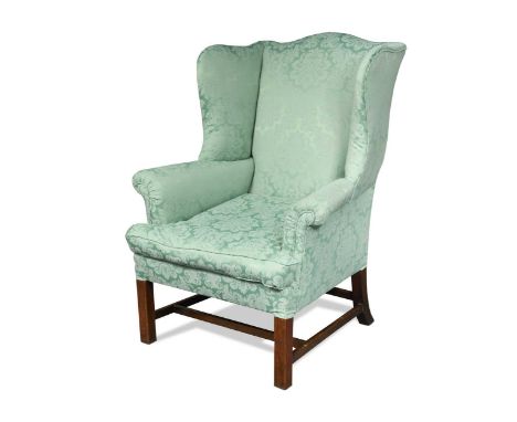 A George III mahogany wing back armchair, the serpentine headed padded back with shaped sides over outscrolling arms and sing
