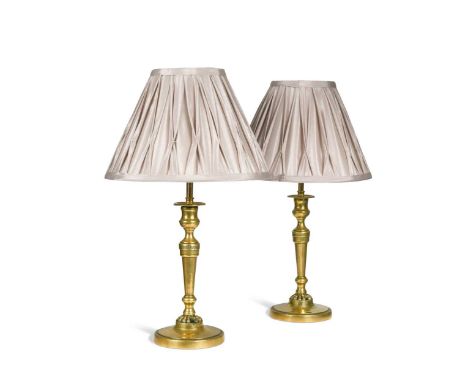 A pair of brass candlestick lamps, early 19th century, with modern conversion to electricity and pleated silk shades36cm to t