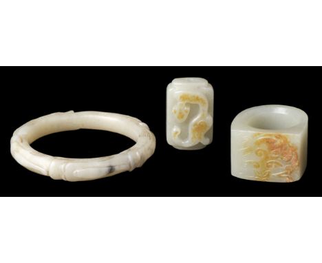 * Jade. A Chinese jade archers ring, the flat top carved with a cub, 3.5 cm across, together with a jade bangle carved with d