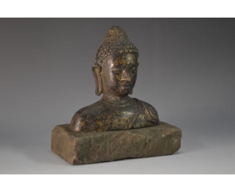 An Asian bronze sculptural fragment, head and bust of Buddha, 10cm wide, rustic stone base