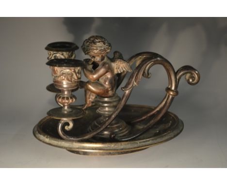 A 19th century dark patinated bronze figural two-light chamberstick, surmounted by a scantily clad putto playing a pipe, camp
